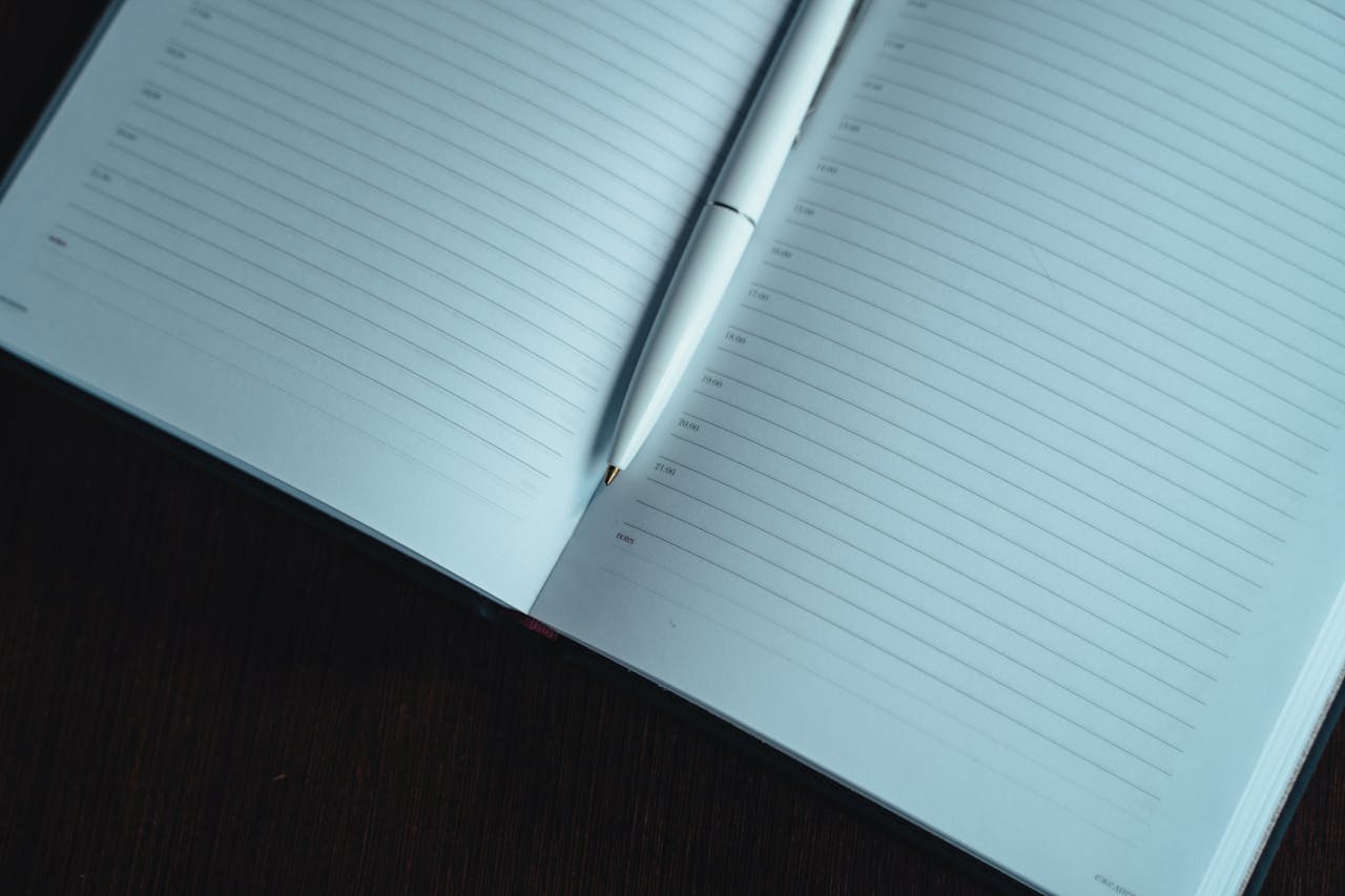 A neatly lined open notebook with a white pen on a dark wooden table, ready for notes.